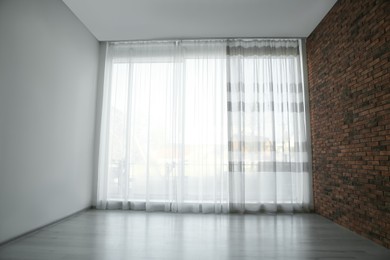 Photo of Empty room with red brick wall, large window and wooden floor