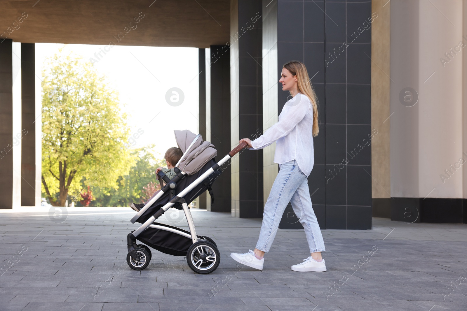 Photo of Happy nanny with cute little boy in stroller walking outdoors