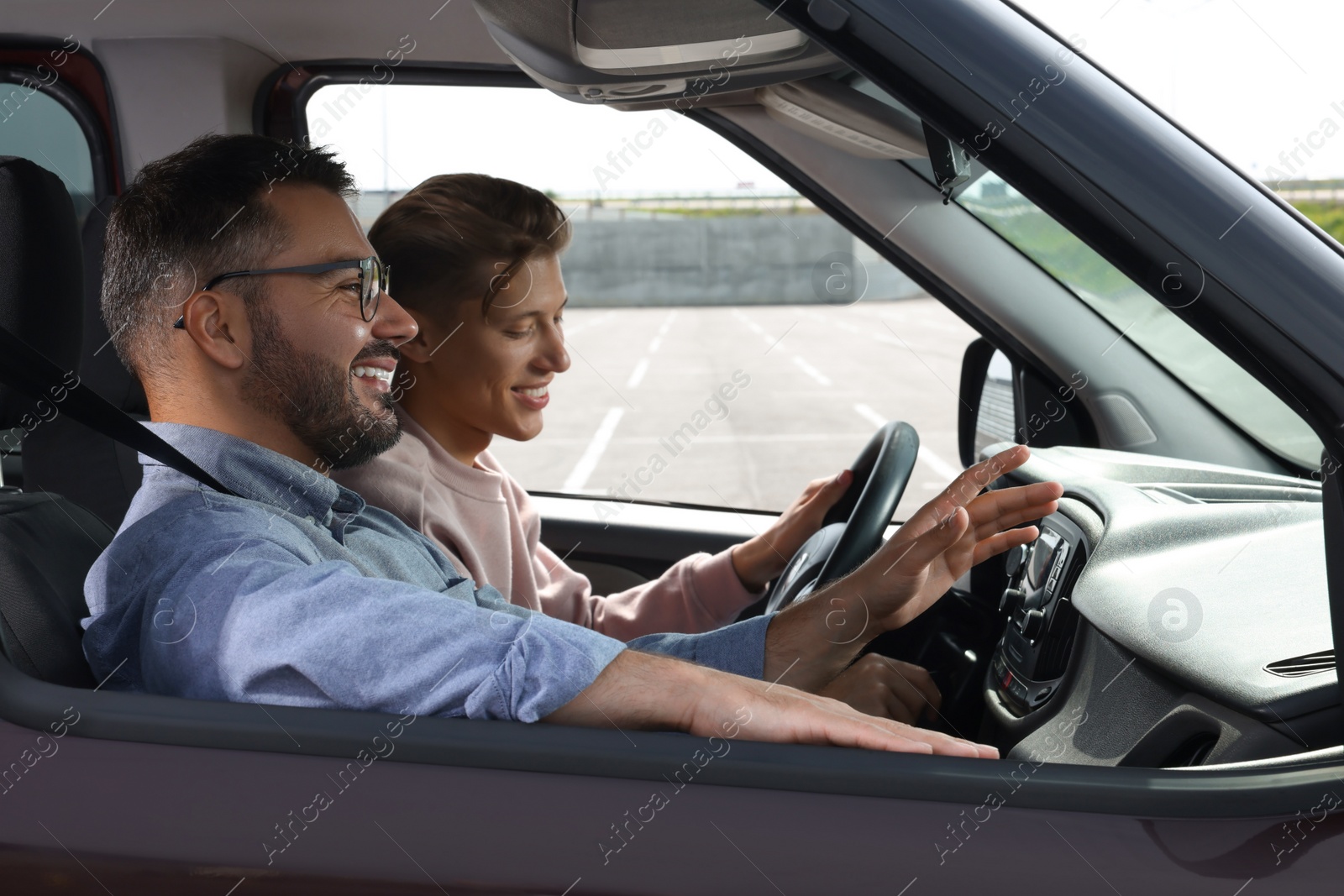 Photo of Driving school. Happy student during lesson with driving instructor in car at parking lot