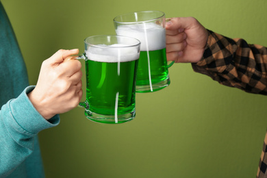 Photo of Man and woman toasting with green beer on color background, closeup. St. Patrick's Day celebration