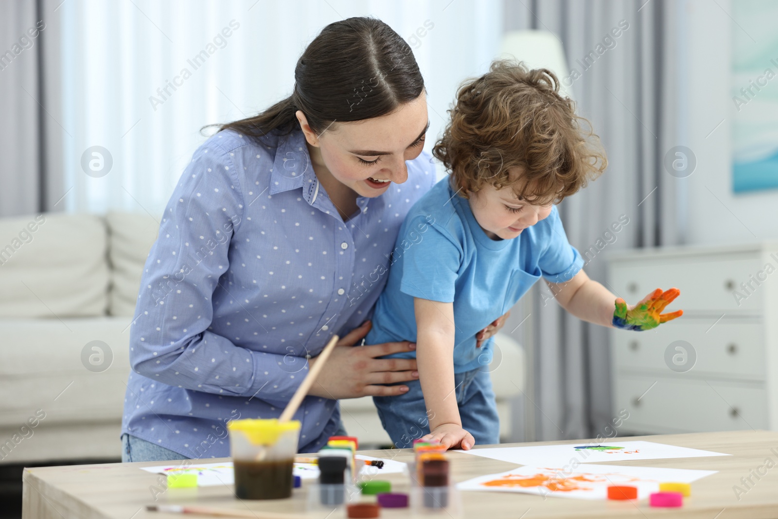 Photo of Mother and her little son painting with palms at home