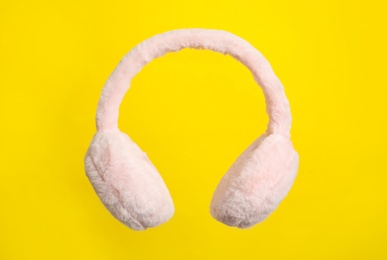 Photo of Fluffy earmuffs on yellow background. Stylish winter accessory