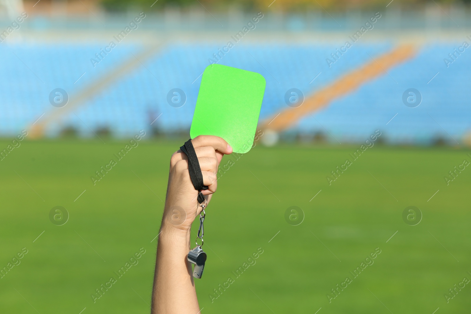 Photo of Football referee holding green card and whistle at stadium, closeup