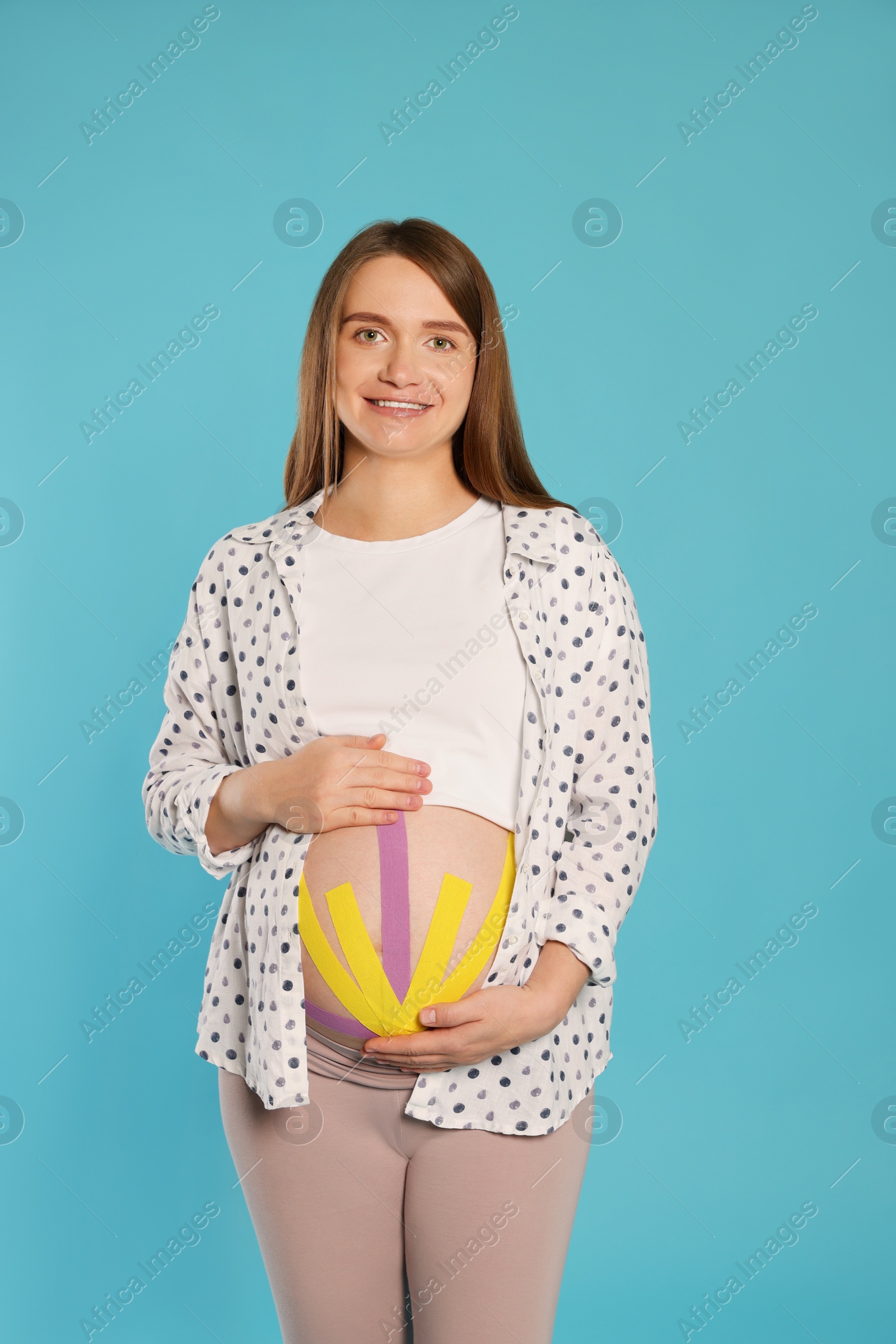 Photo of Pregnant woman with kinesio tapes on her belly against light blue background