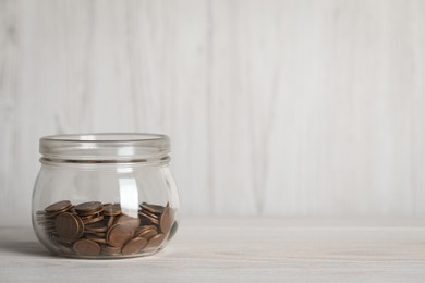 Photo of Glass jar with coins on white wooden table. Space for text