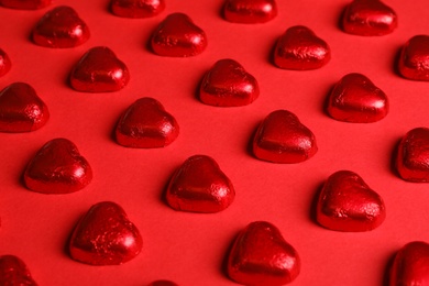 Tasty chocolate heart shaped candies on red background