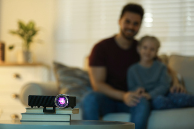 Photo of Young man and her daughter watching movie at home, focus on video projector