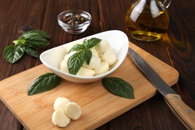 Photo of Tasty mozarella balls, basil leaves and knife on wooden table