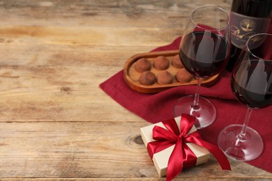 Photo of Red wine, chocolate truffles and gift box on wooden table. Space for text