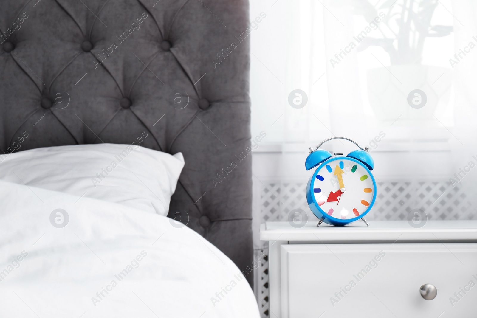 Photo of Analog alarm clock on table in bedroom. Time of day