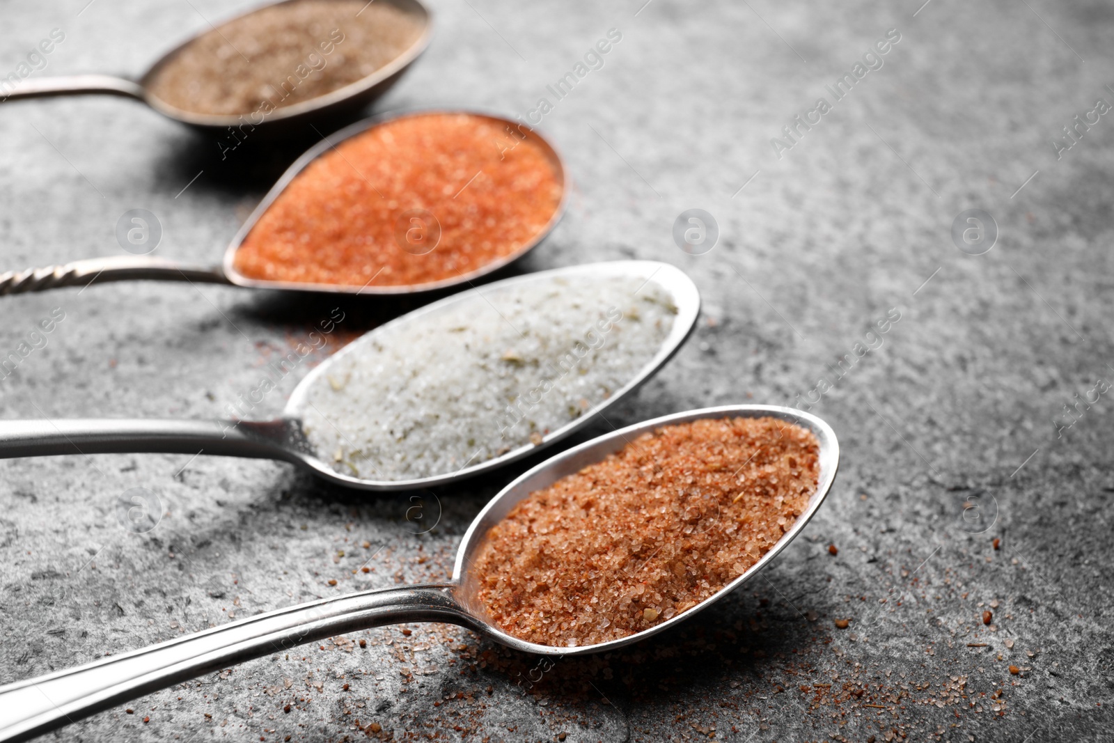 Photo of Spoons with different kinds of salt on grey table