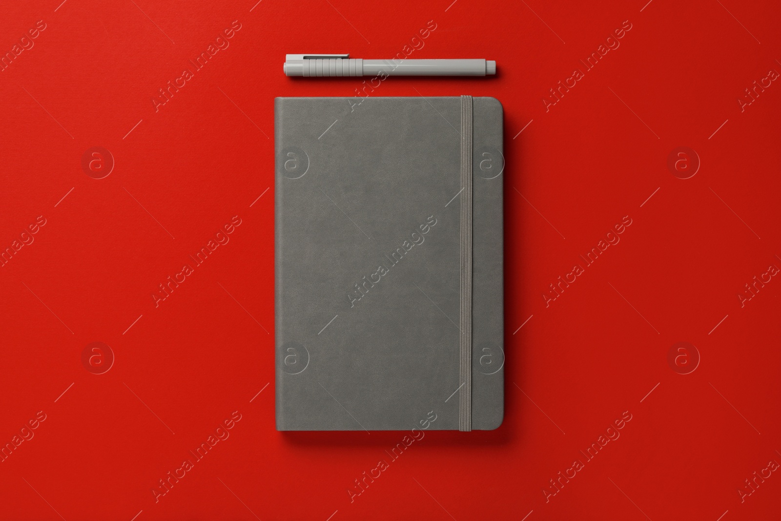 Photo of Gray notebook and pen on red background, flat lay