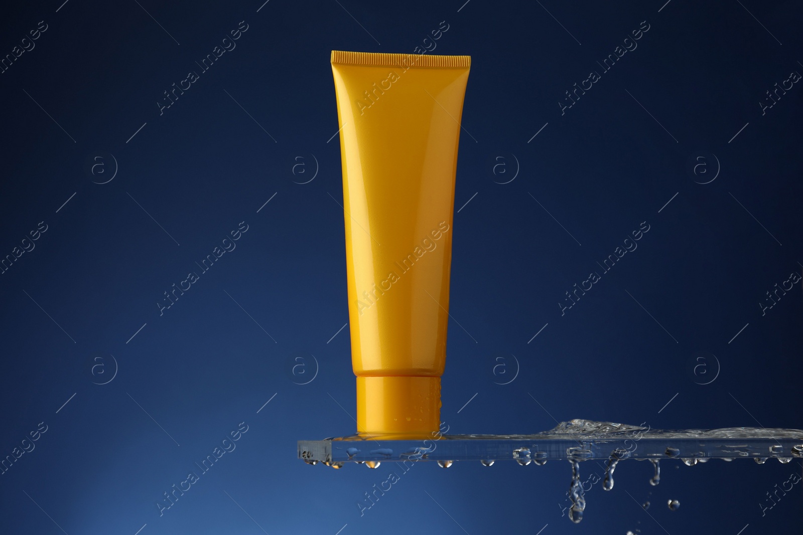 Photo of Moisturizing cream in tube on glass with water drops against blue background. Space for text