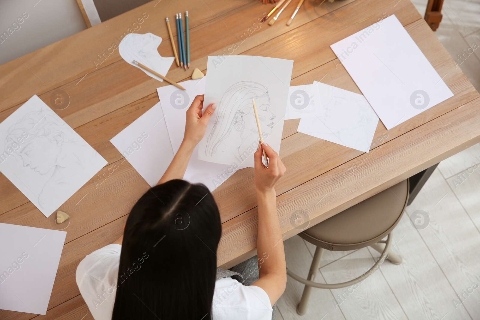 Photo of Young woman drawing male portrait at table indoors, above view