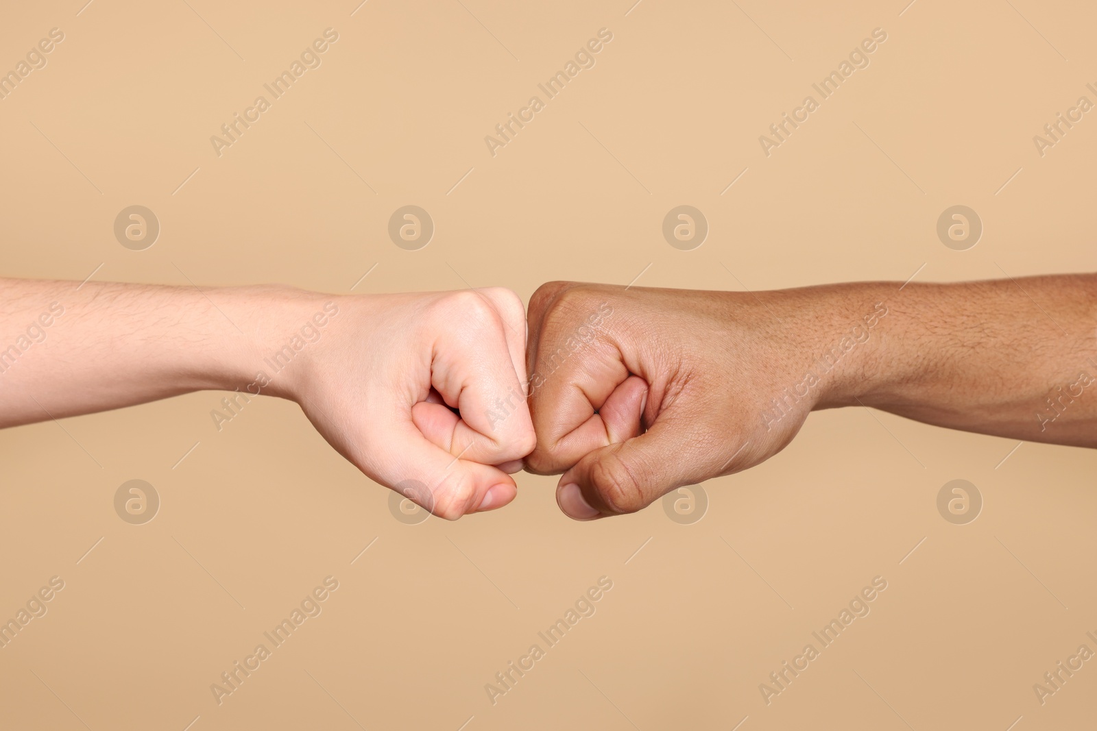 Photo of International relationships. People making fist bump on light brown background, closeup
