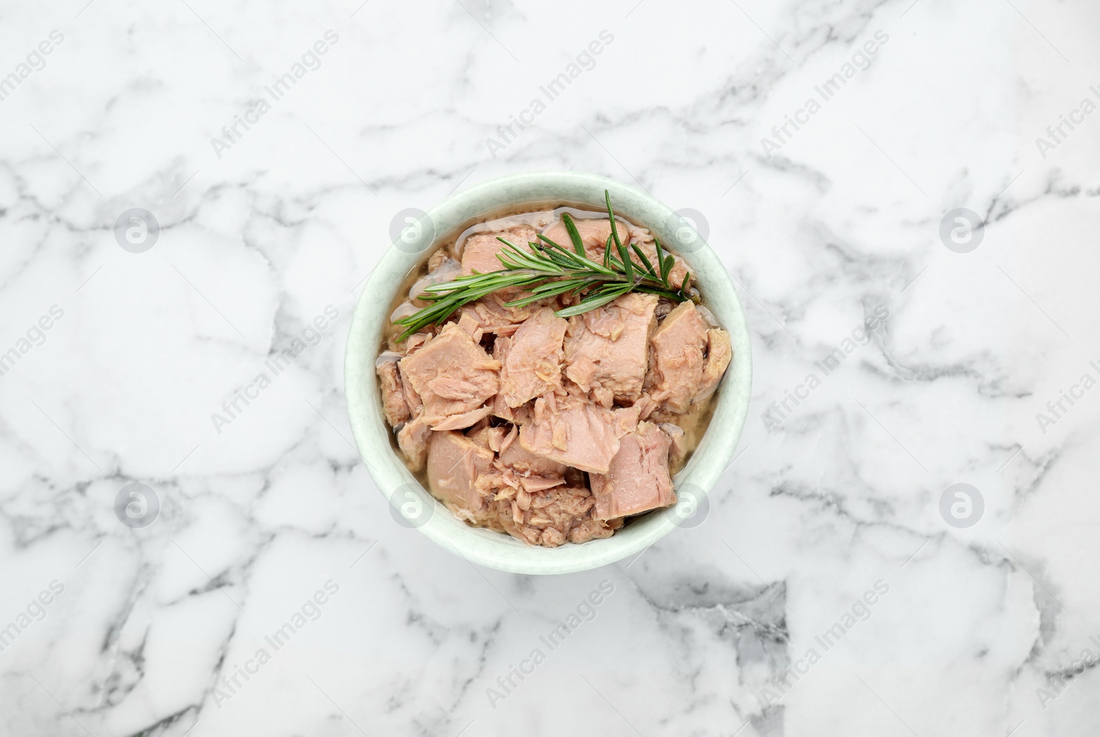 Photo of Bowl with canned tuna and rosemary on white marble table, top view