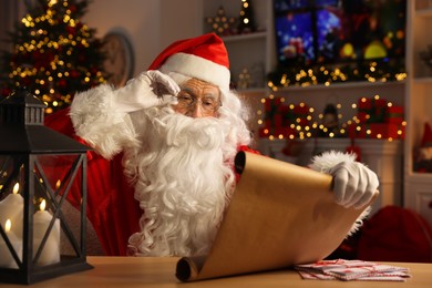 Photo of Santa Claus reading letter at table in room decorated for Christmas