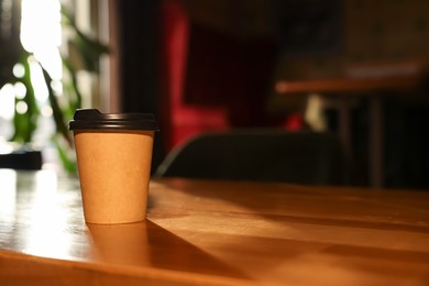 Paper coffee cup on wooden table in cafe. Space for text