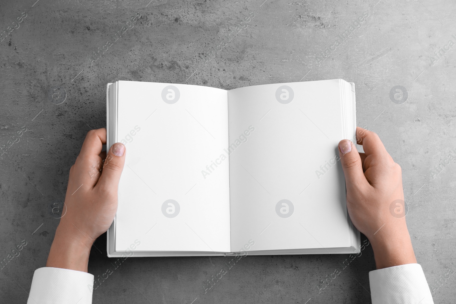 Photo of Man holding blank book at grey table, top view. Mock up for design