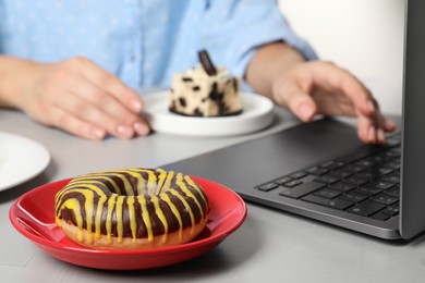 Photo of Bad habits. Woman eating different snacks while using laptop at grey table, selective focus