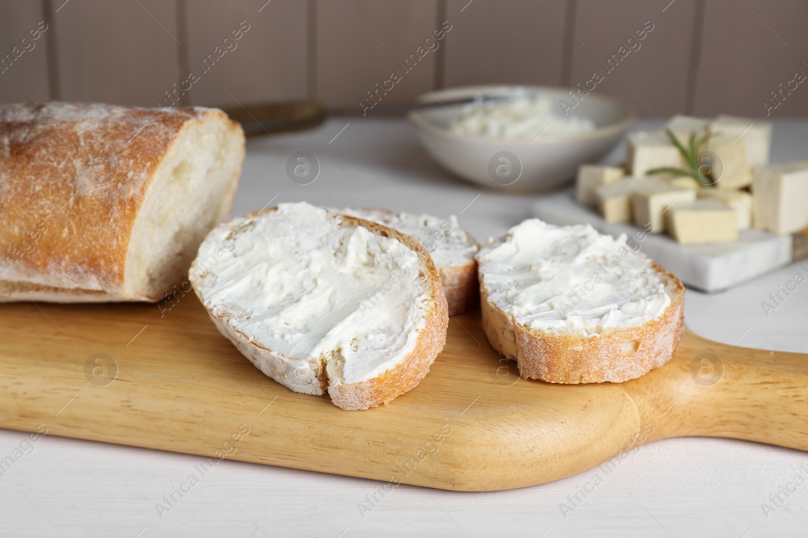 Photo of Slices of baguette with tofu cream cheese on white wooden table