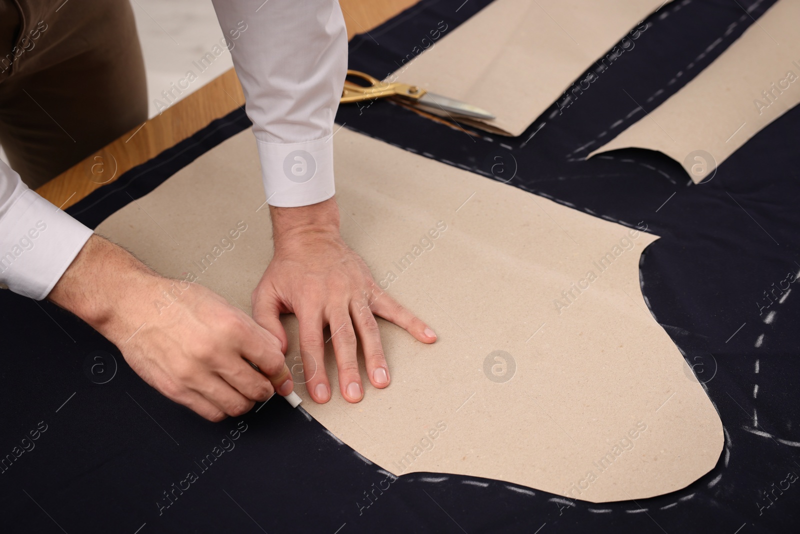 Photo of Tailor marking sewing pattern on fabric with chalk at table, closeup