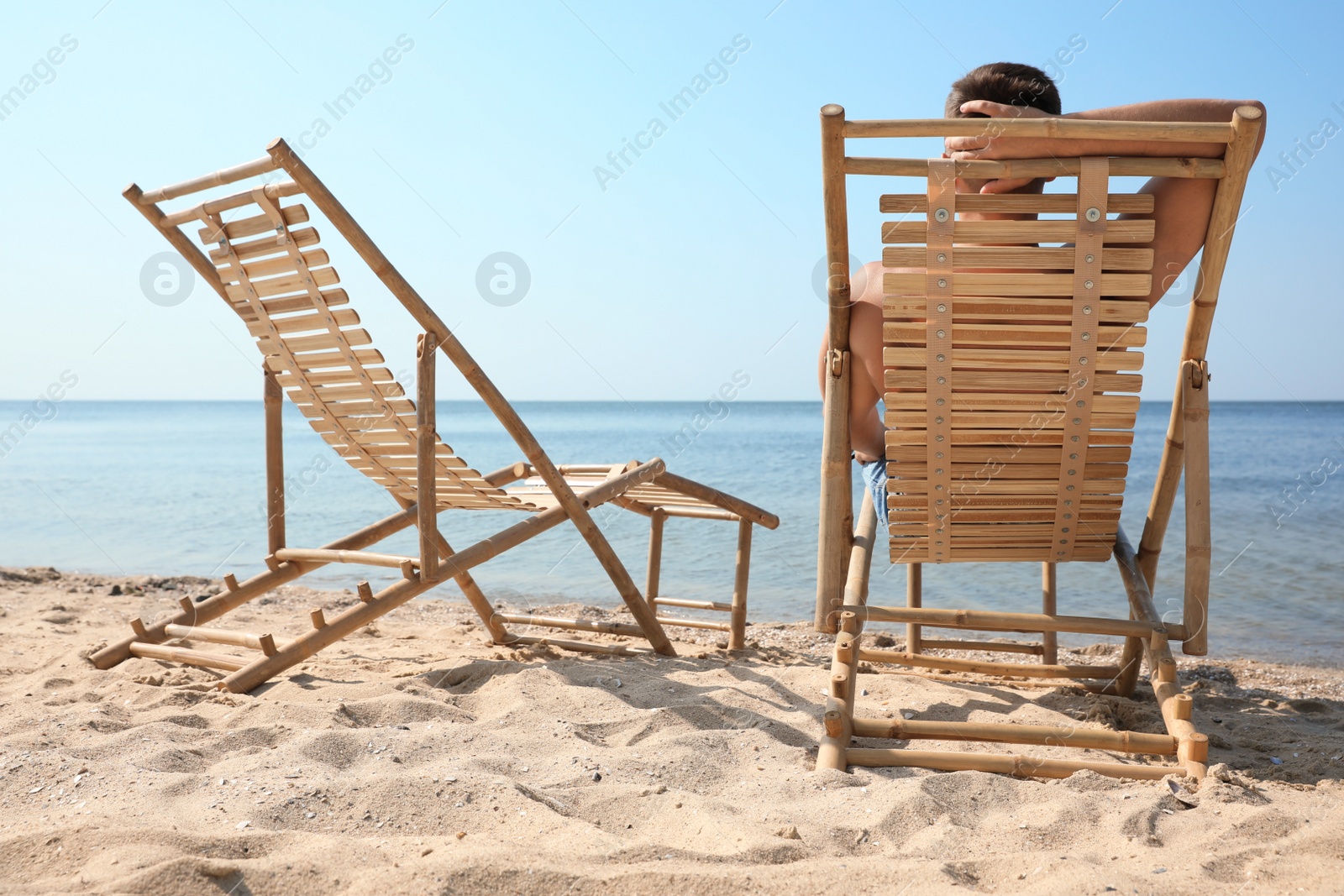 Photo of Young man relaxing in deck chair on sandy beach