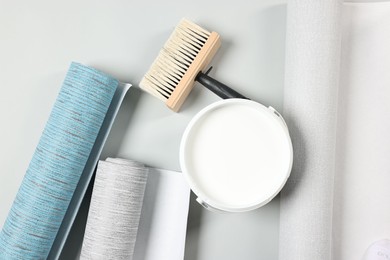 Photo of Different wallpaper rolls, brush and bucket with glue on light background, flat lay