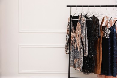 Photo of Collection of trendy women's garments on rack near white wall indoors, space for text. Clothing rental service