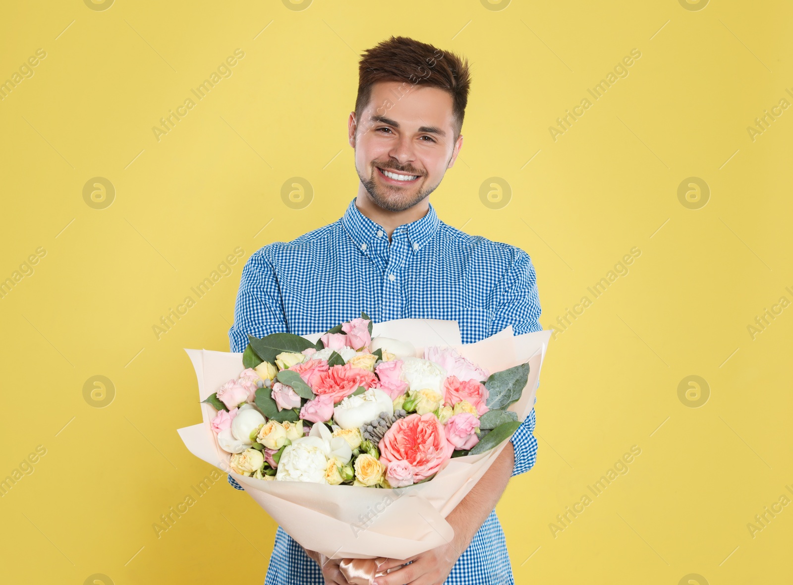 Photo of Young handsome man with beautiful flower bouquet on yellow background