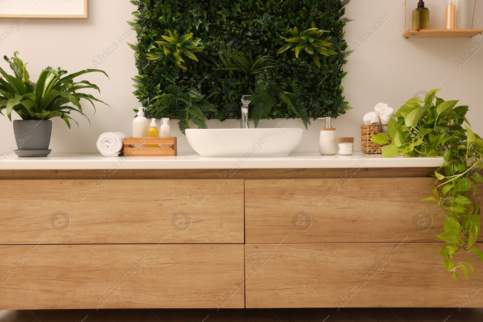 Photo of Green artificial plants, vanity and different personal care products in bathroom