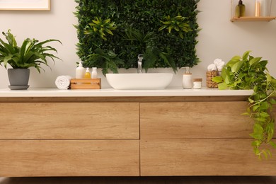 Green artificial plants, vanity and different personal care products in bathroom