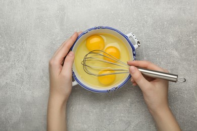 Photo of Woman whisking eggs at grey table, top view