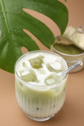 Glass of tasty iced matcha latte and leaf on light brown background