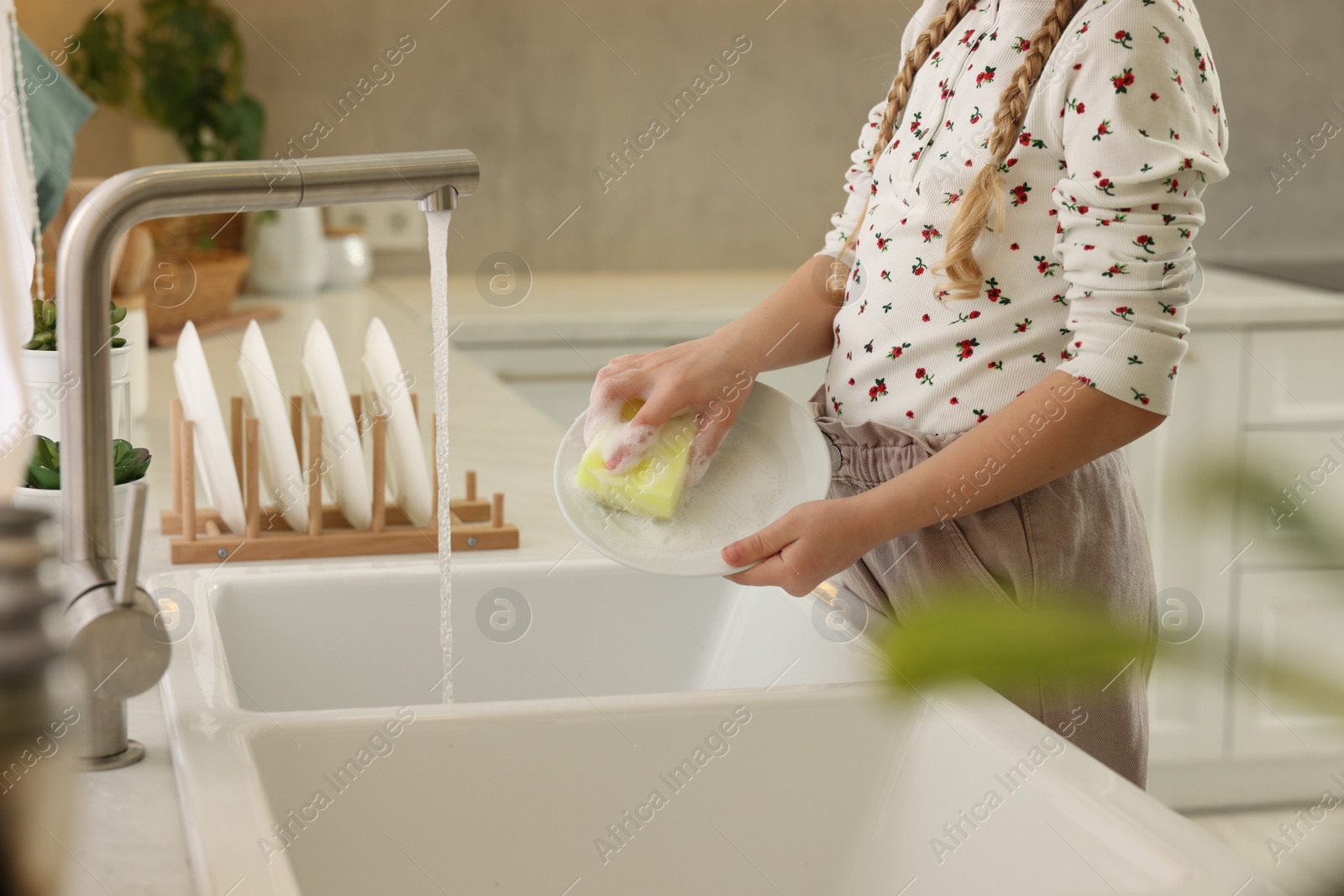 Photo of Little girl washing plate above sink in kitchen, closeup