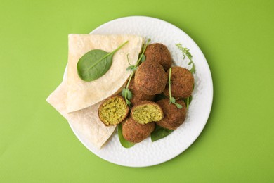 Photo of Delicious falafel balls, herbs and lavash on green background, top view