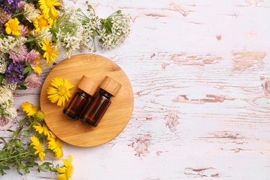 Photo of Bottles of essential oils and beautiful flowers on white wooden table, flat lay. Space for text