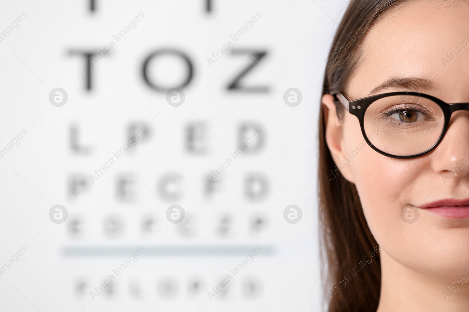 Photo of Young woman with glasses against vision test chart, closeup