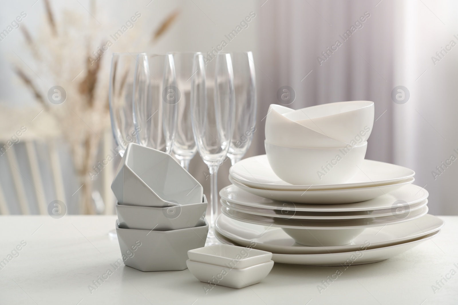 Photo of Set of clean dishware and champagne glasses on white table indoors