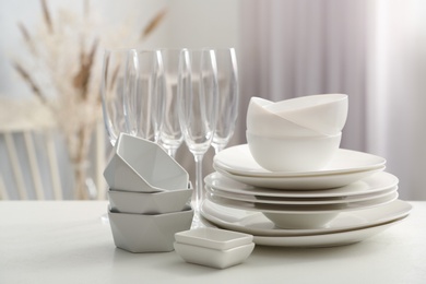 Set of clean dishware and champagne glasses on white table indoors