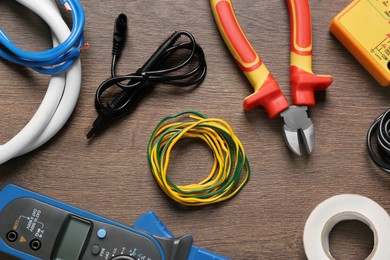 Different wires and electrician's tools on wooden table, flat lay