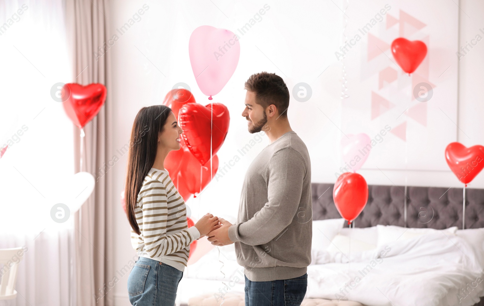 Photo of Lovely young couple in bedroom decorated with heart shaped balloons. Valentine's day celebration