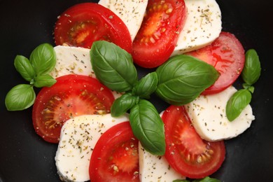 Photo of Caprese salad with tomatoes, mozzarella, basil and spices in bowl, top view