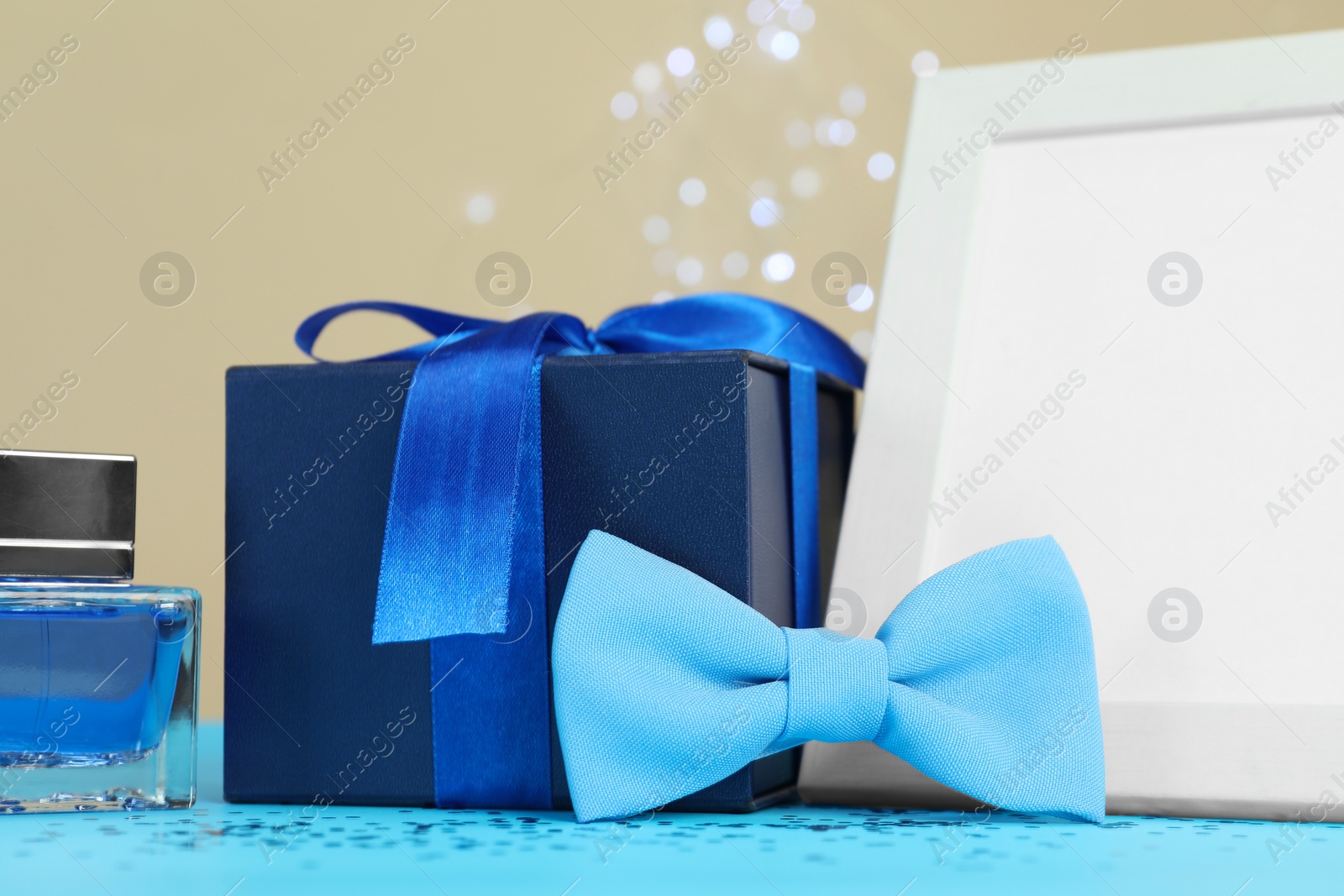 Photo of Happy Father's Day. Empty frame, bow tie, perfume and gift box on light blue table, closeup. Space for text