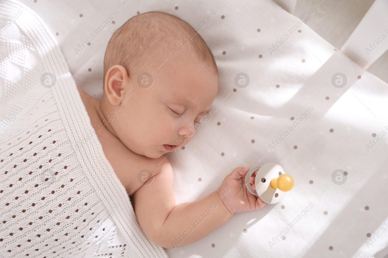 Photo of Cute little baby with pacifier sleeping in crib, top view