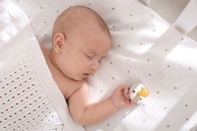 Cute little baby with pacifier sleeping in crib, top view