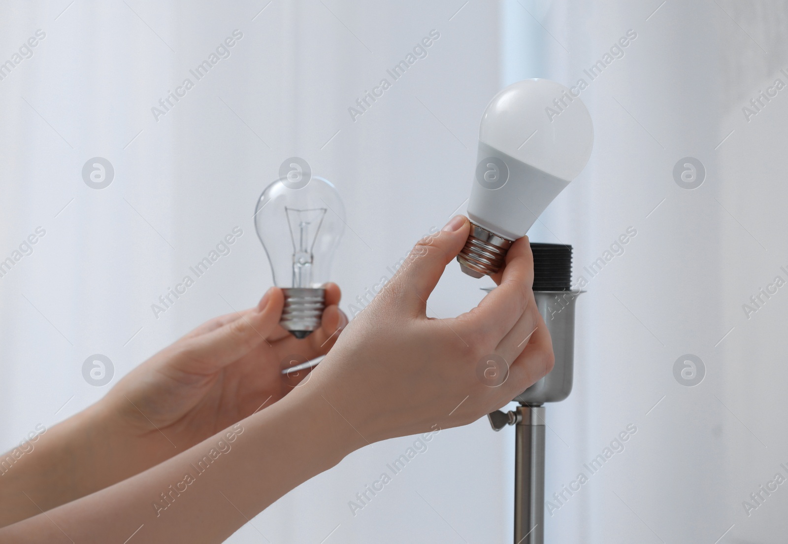 Photo of Woman changing incandescent light bulb for fluorescent one in lamp at home, closeup. Saving energy concept