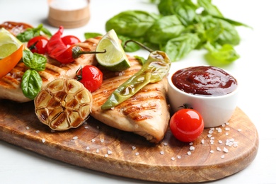 Photo of Tasty grilled chicken fillets with sauce, vegetables and lime on wooden board, closeup