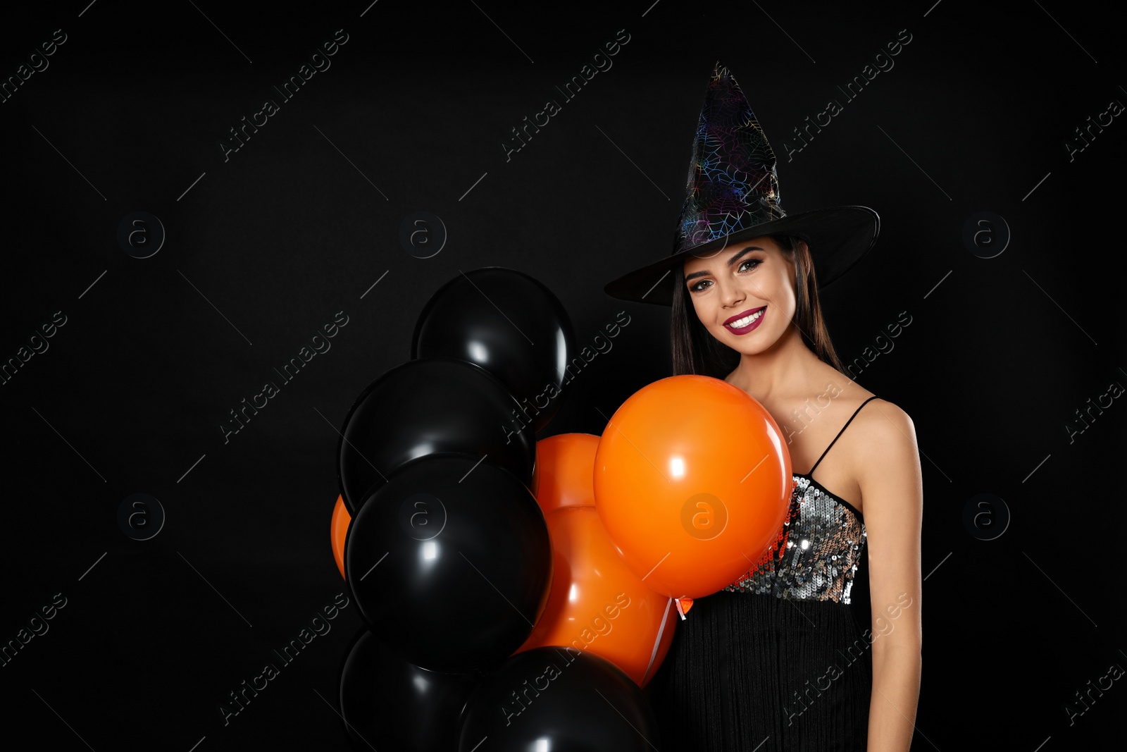 Photo of Beautiful woman wearing witch costume with balloons for Halloween party on black background