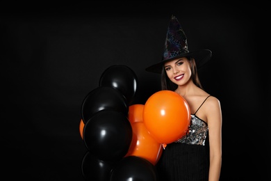 Photo of Beautiful woman wearing witch costume with balloons for Halloween party on black background